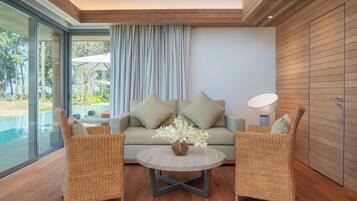 Un salon moderne avec un canapé, deux fauteuils en osier, une table basse ronde et une vue sur une piscine.
