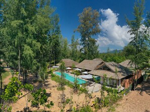 A resort with multiple bungalow-style buildings, a swimming pool, and a mountainous backdrop.