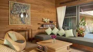 A modern living room with a wooden floor, a sofa with cushions, a coffee table, a wicker chair, a bookshelf, and a large abstract painting.