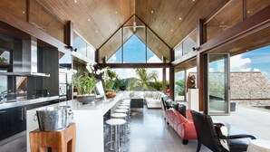 A modern kitchen with a central island, bar stools, and a seating area with a red sofa and black chairs. - Suralai by Elite Havens (Koh Samui)
