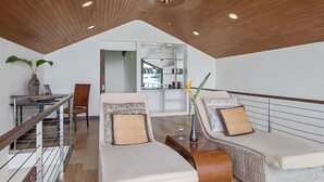 Un dormitorio estilo loft moderno con techo alto, una escalera de cristal, un rincón de descanso con cojines y una estantería.