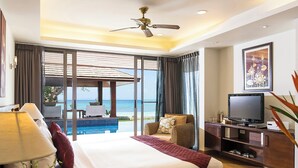 Un cuarto de hotel con una cama grande, un televisor, un escritorio con una silla, un balcón con vista al océano y un ventilador de techo.