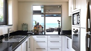 Cocina moderna con vista al océano, que incluye electrodomésticos de acero inoxidable, armarios blancos y un comedor con vistas.