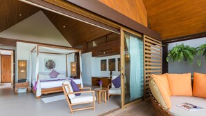 A spacious bedroom with a four-poster bed, a sitting area with a sofa and chairs, and a large window with a view of the outdoors. - Baan Puri (Koh Samui)