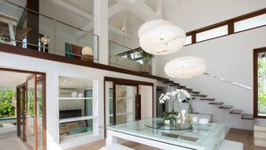 A modern interior with a glass dining table, white benches, and two large, round, white pendant lights. - Ban Suriya (Koh Samui)