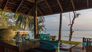 A wooden deck with a thatched roof, outdoor seating with cushions, a lantern, and a view of the sea. - Villa Waimarie (Koh Samui)