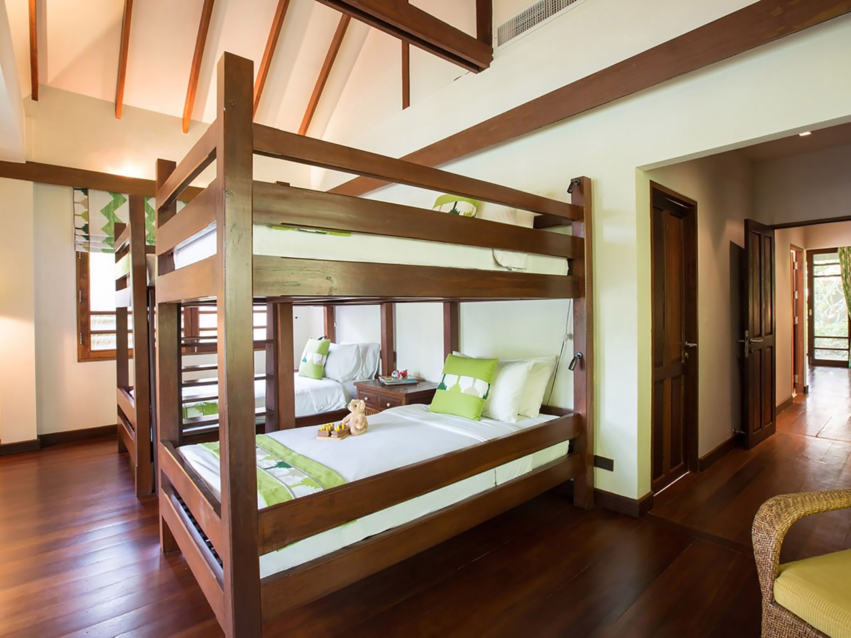 Quarto com beliche, vigas de madeira, colcha verde e branca e uma cadeira de vime.