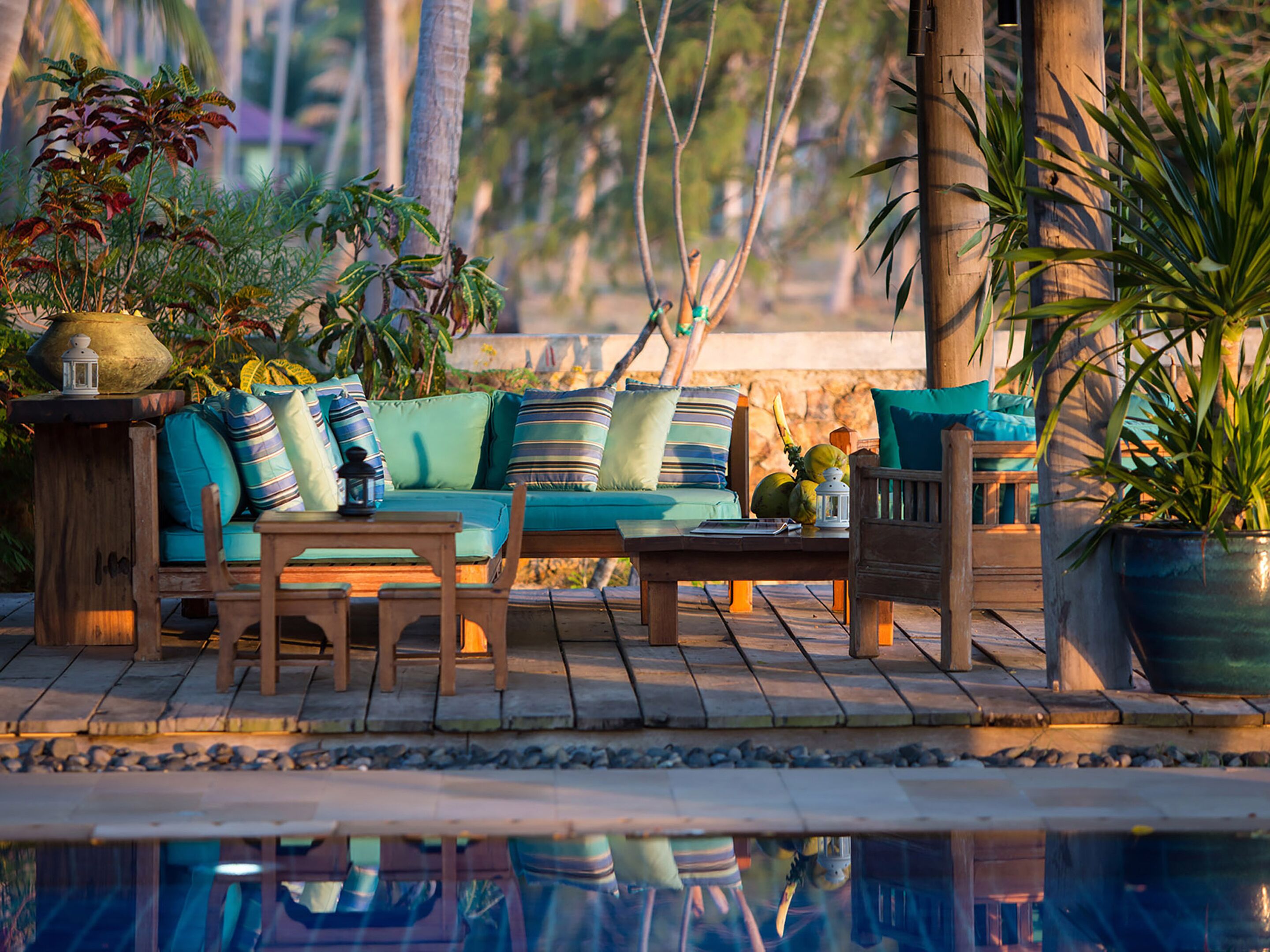 A wooden deck with a sofa, chairs, and a table. There are potted plants and a lantern on the deck.