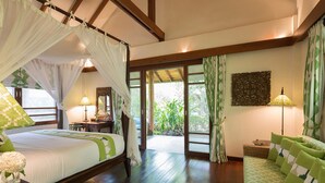 A spacious bedroom with a canopy bed, a wooden floor, a green sofa, and a view of the garden through the sliding glass door. - Villa Waimarie (Koh Samui)