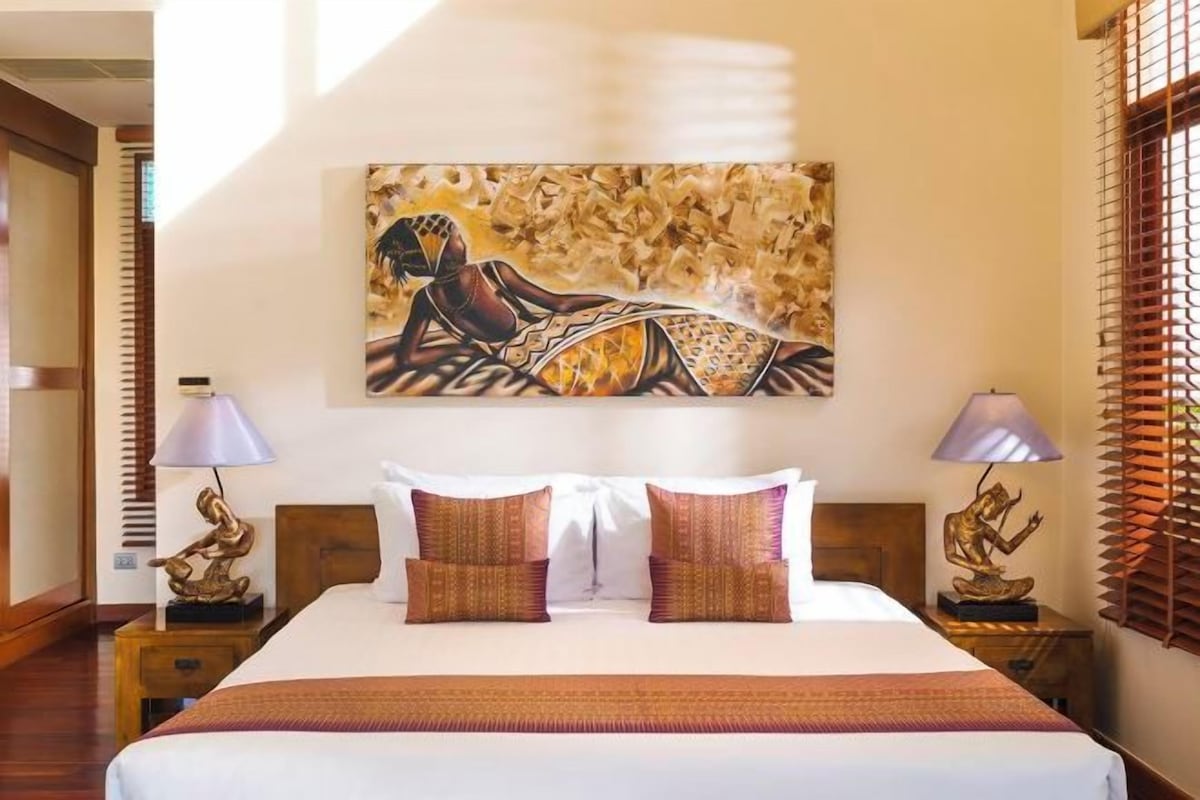 A hotel room with a large bed, two nightstands, a wall painting, and a window with blinds.