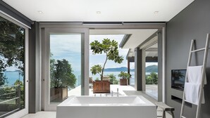 A modern bathroom with a large bathtub, a wooden bench, and a TV mounted on the wall. - Cape Laem Sor Estate (Koh Samui)