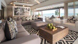 A spacious living area with a high ceiling, large windows offering a view of the sea, and a modern design with a mix of sofas and a coffee table. - Cape Laem Sor Estate (Koh Samui)