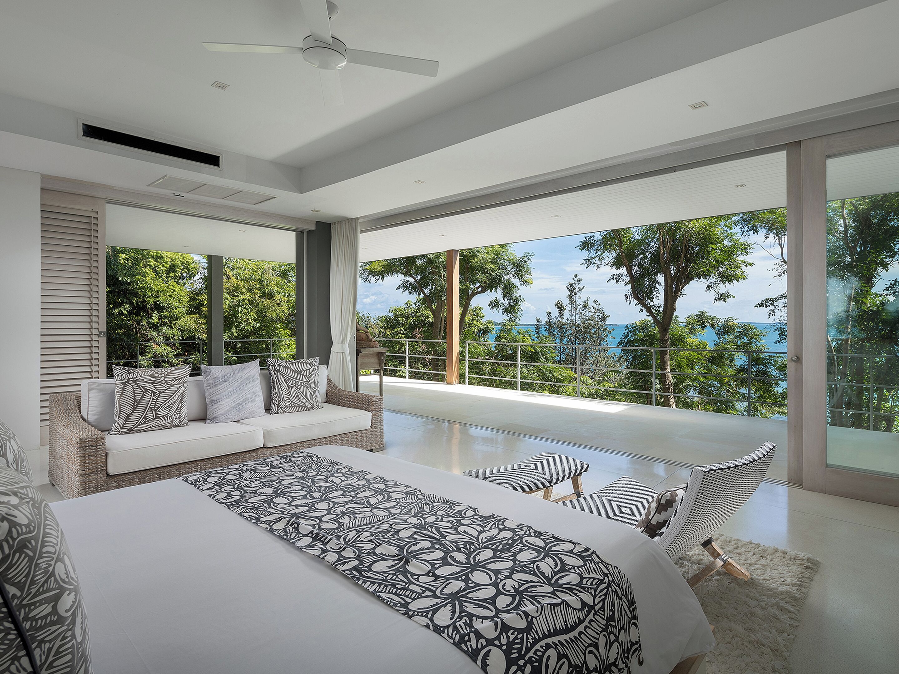 A modern bedroom with a large bed, a sofa, and a view of the ocean.