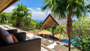 A balcony with wicker furniture, a pool, and a view of the ocean. - Panacea Retreat (Koh Samui)