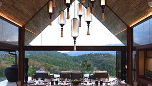A dining area with a high ceiling, large windows, and a view of a mountainous landscape. - Panacea Retreat (Koh Samui)