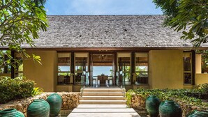 A building with a tiled roof, a stone pathway leading to a glass door, and large green planters on either side. - Panacea Retreat (Koh Samui)