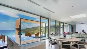 Ein moderner Essbereich mit weitreichendem Meerblick, einer verglasten Terrasse und einem runden Tisch mit Stühlen.