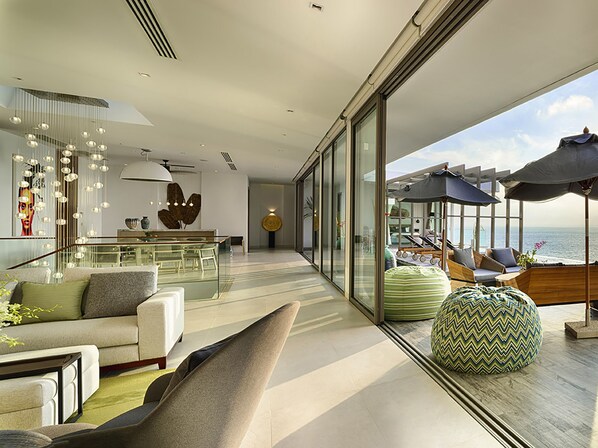 Una sala de estar moderna con un amplio ventanal, un comedor y una zona de estar con vistas al océano.