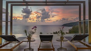 Ein Zimmer mit Meerblick bei Sonnenuntergang, ausgestattet mit drei Liegestühlen und zwei Blumentöpfen.