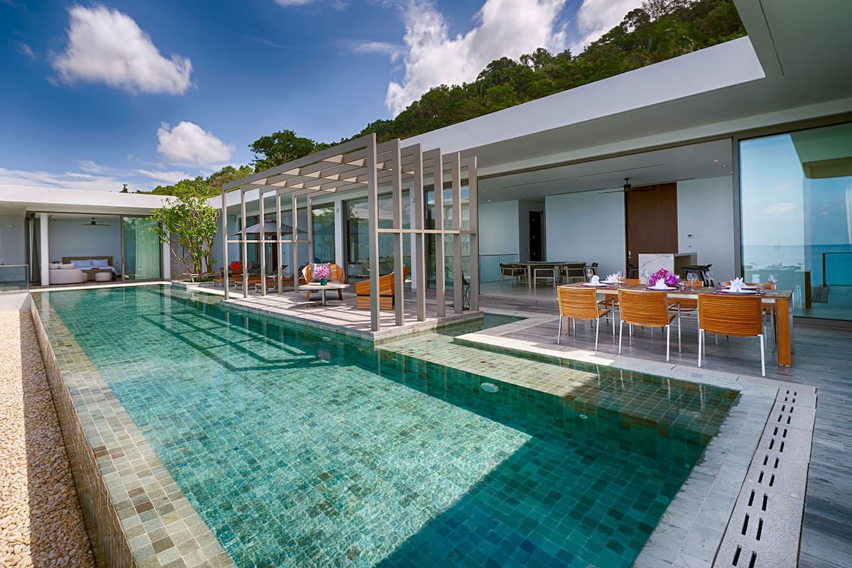 A modern poolside area with a clear pool, wooden deck, and outdoor seating.