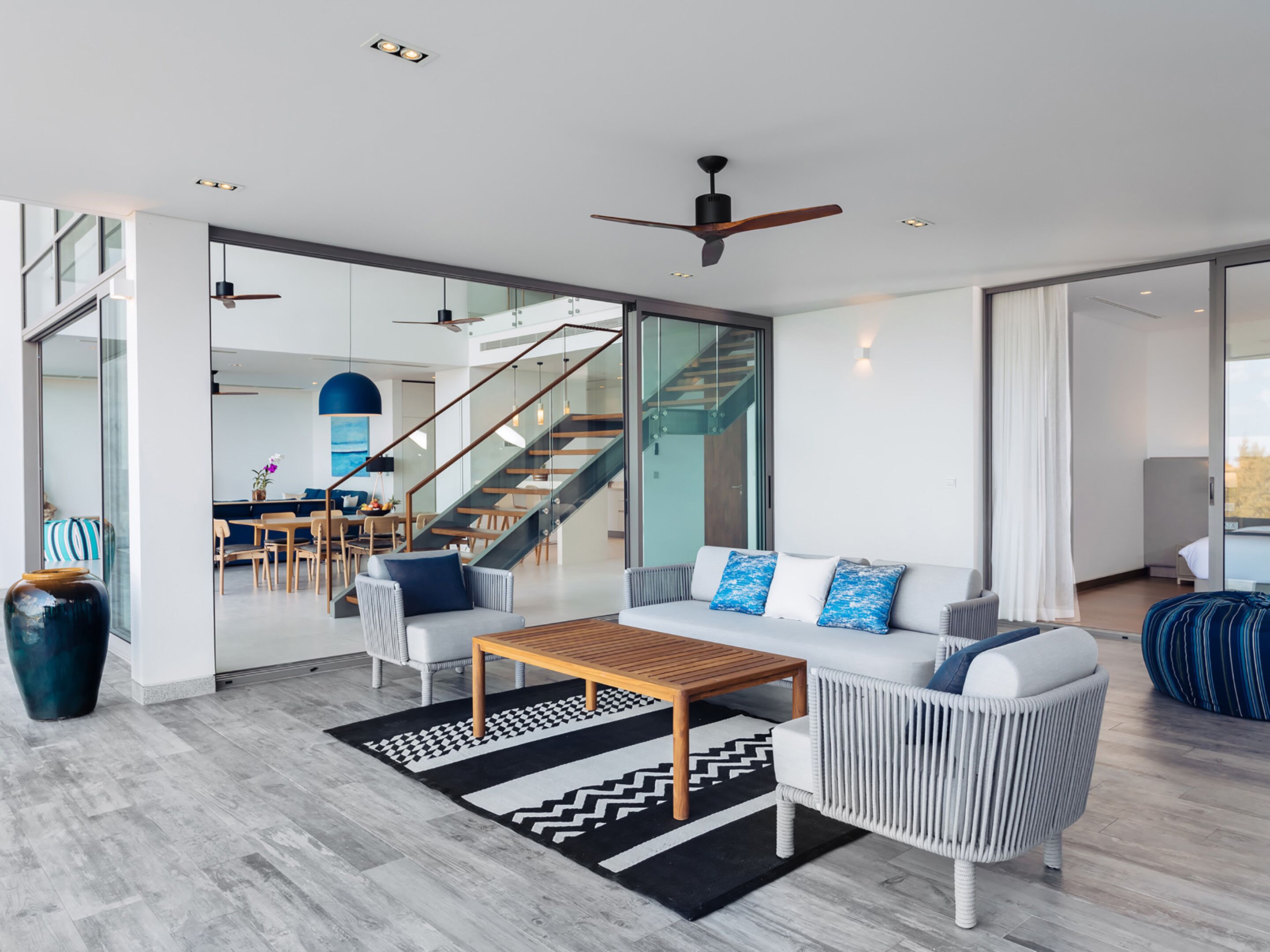 Una sala moderna con un sofá, una mesa de centro y un tapete estampado. Una escalera conduce a un nivel superior.