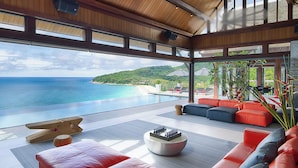 Ein modernes Wohnzimmer mit einem großen Fenster, das einen Pool und eine schöne Aussicht auf Meer und Hügel zeigt.