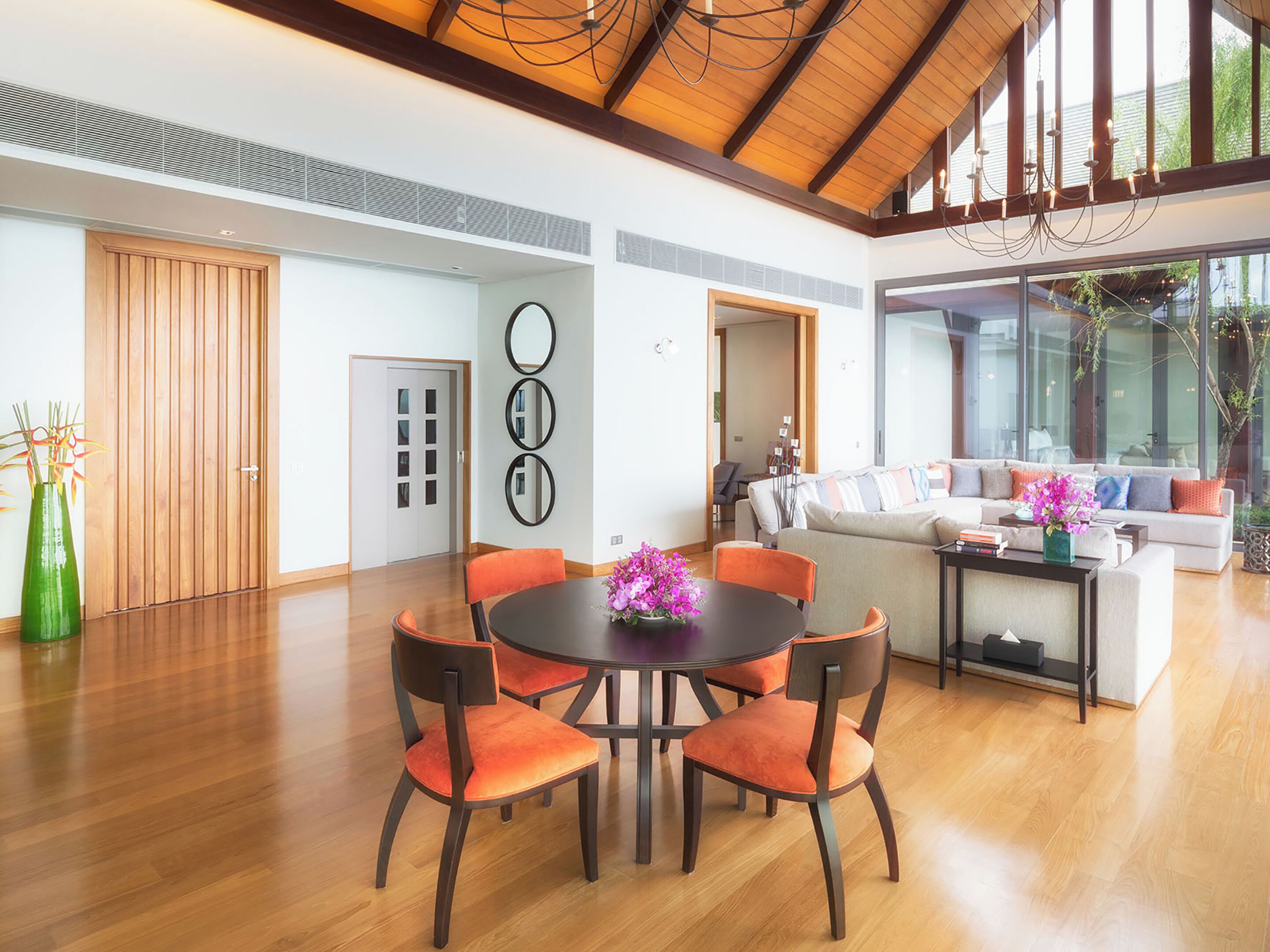 Un amplio salón con techo de madera, una mesa de comedor con sillas anaranjadas y un sofá con cojines coloridos.