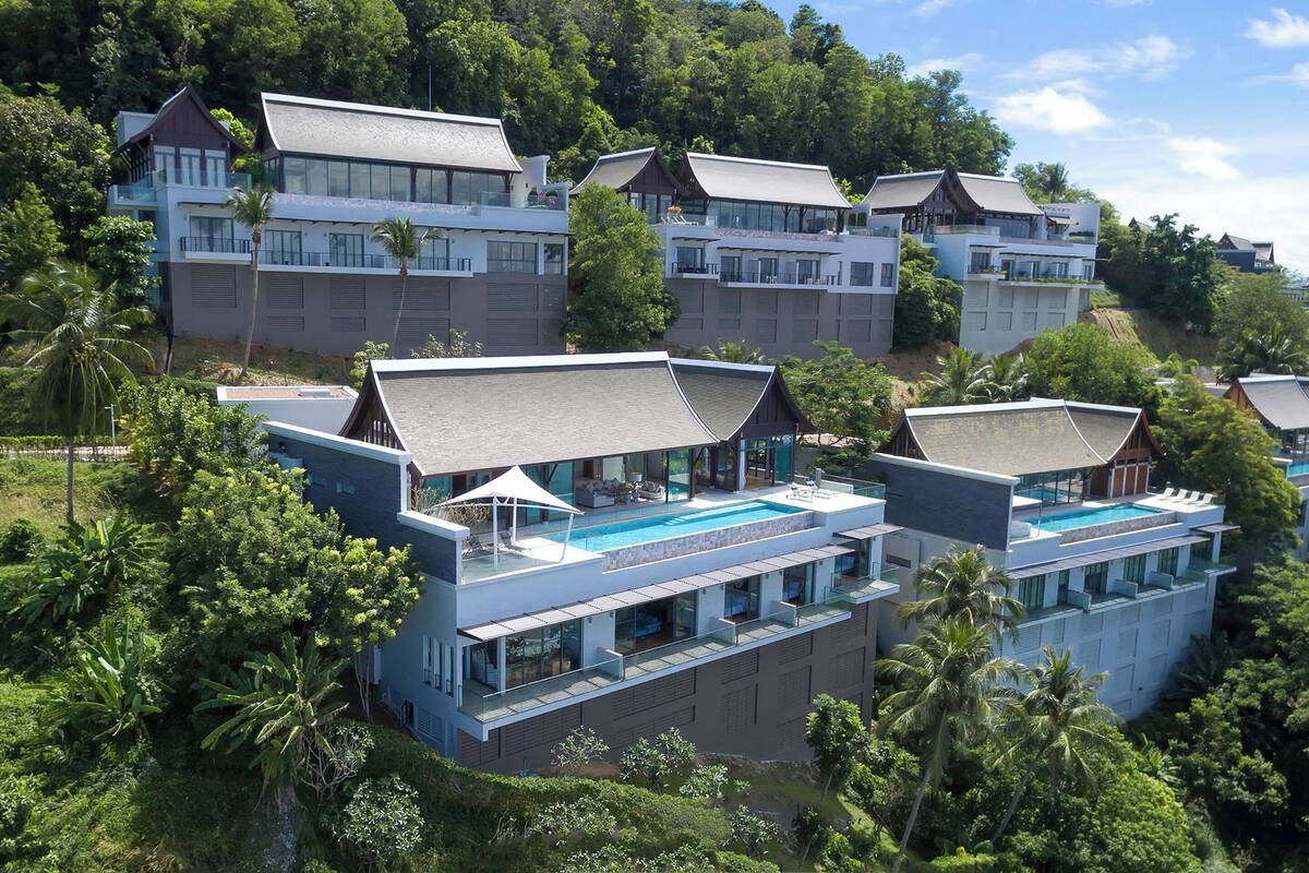 A resort with multiple modern buildings, a large swimming pool, and lush greenery surrounding the property.