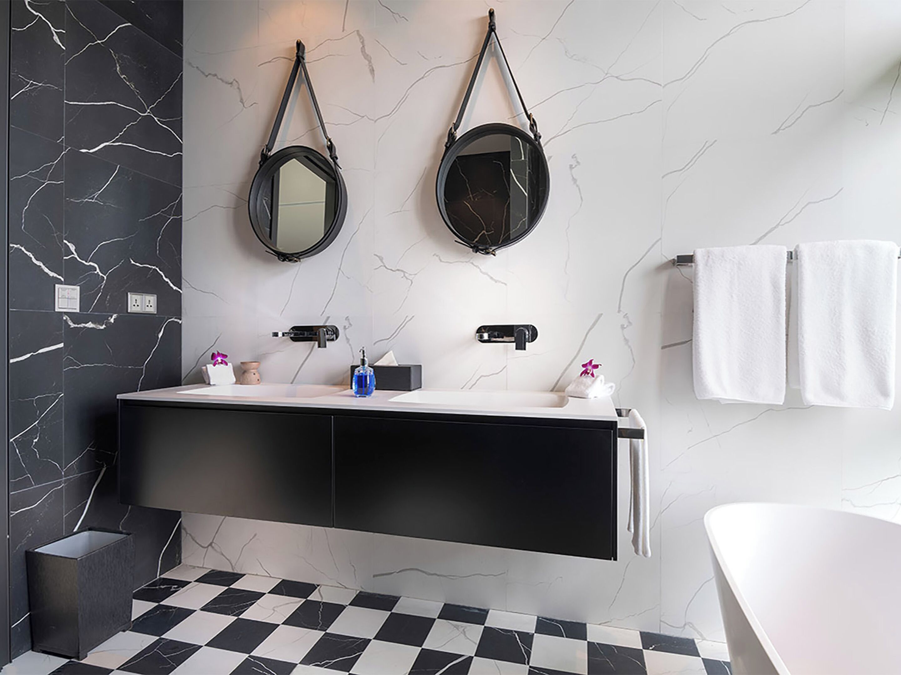 A modern bathroom with a black and white checkered floor, a black vanity with two sinks, a white bathtub, and two wall-mounted mirrors.