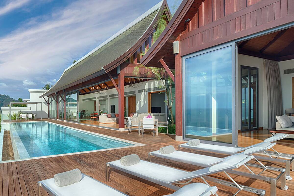 A modern poolside area with lounge chairs, a covered seating area, and a glass-enclosed room.