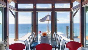 Ein Essbereich mit Glastisch und Stühlen, mit Blick auf das Meer.
