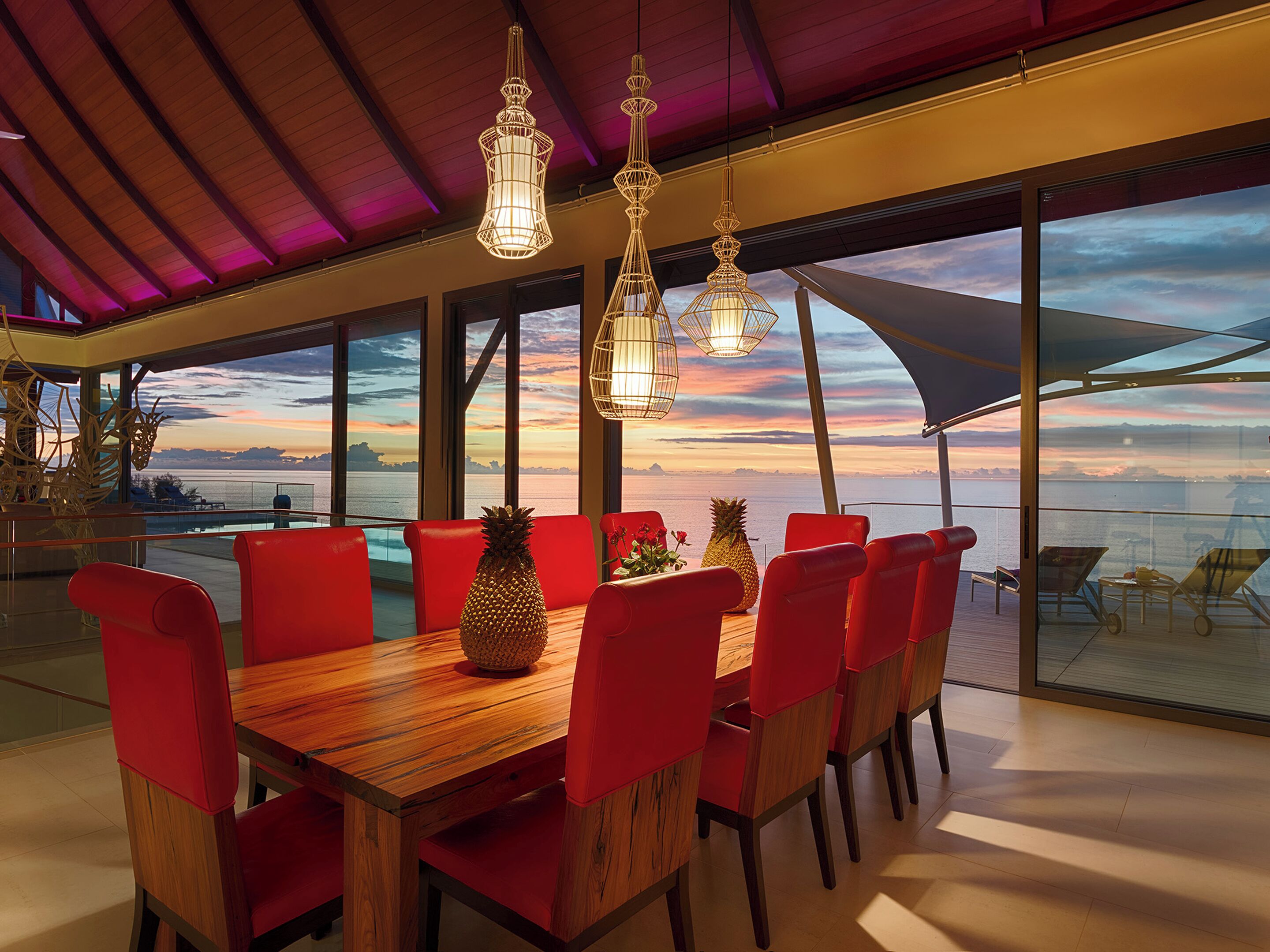 A dining area with a wooden table and red chairs, overlooking a scenic ocean view.
