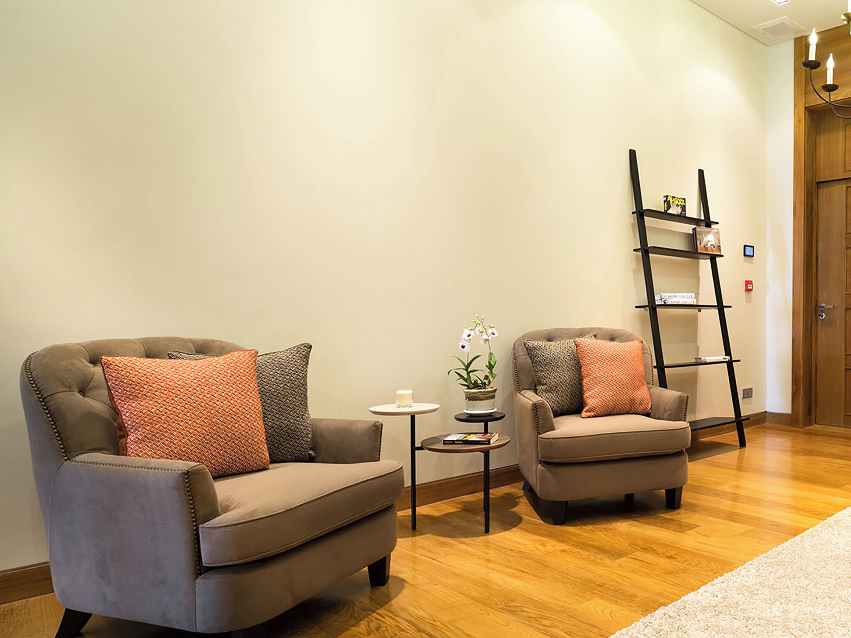 A room with two armchairs, a small table with a candle and a plant, and a wooden floor.