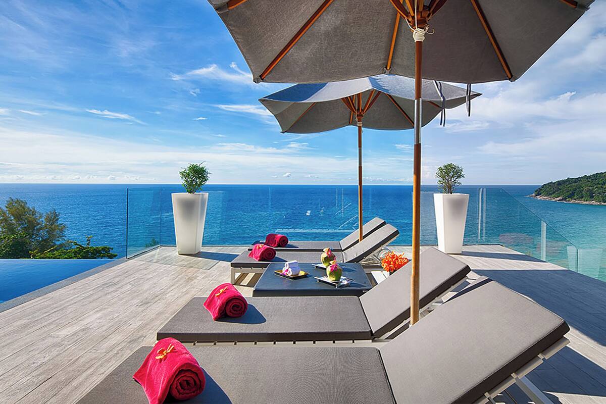 A luxurious outdoor lounge area with a clear view of the ocean, featuring sun loungers, umbrellas, and potted plants.