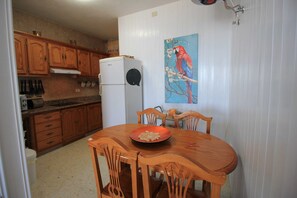 A kitchen with wooden cabinets, a white refrigerator, and a dining table with chairs. - Apartment Maritimo, Spanien (Puerto de Naos)