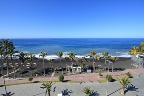 A beach view with palm trees, a sandy area, and a clear blue sky. - Apartment Maritimo, Spanien (Puerto de Naos)