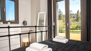 A bedroom with a bed, two windows, a mirror, and a balcony with a view of greenery. - Giannakis Villa (Kerkyra)
