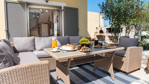 A wicker outdoor seating area with a table set for breakfast, including bread, fruit, and beverages. - Giannakis Villa (Kerkyra)