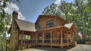 A log cabin with a stone chimney, wooden deck, and an American flag. - Deer Trails Cabin - Blue Ridge (Cherry Log)