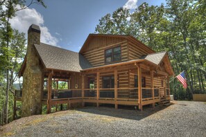 A log cabin with a stone chimney, wooden deck, and an American flag.