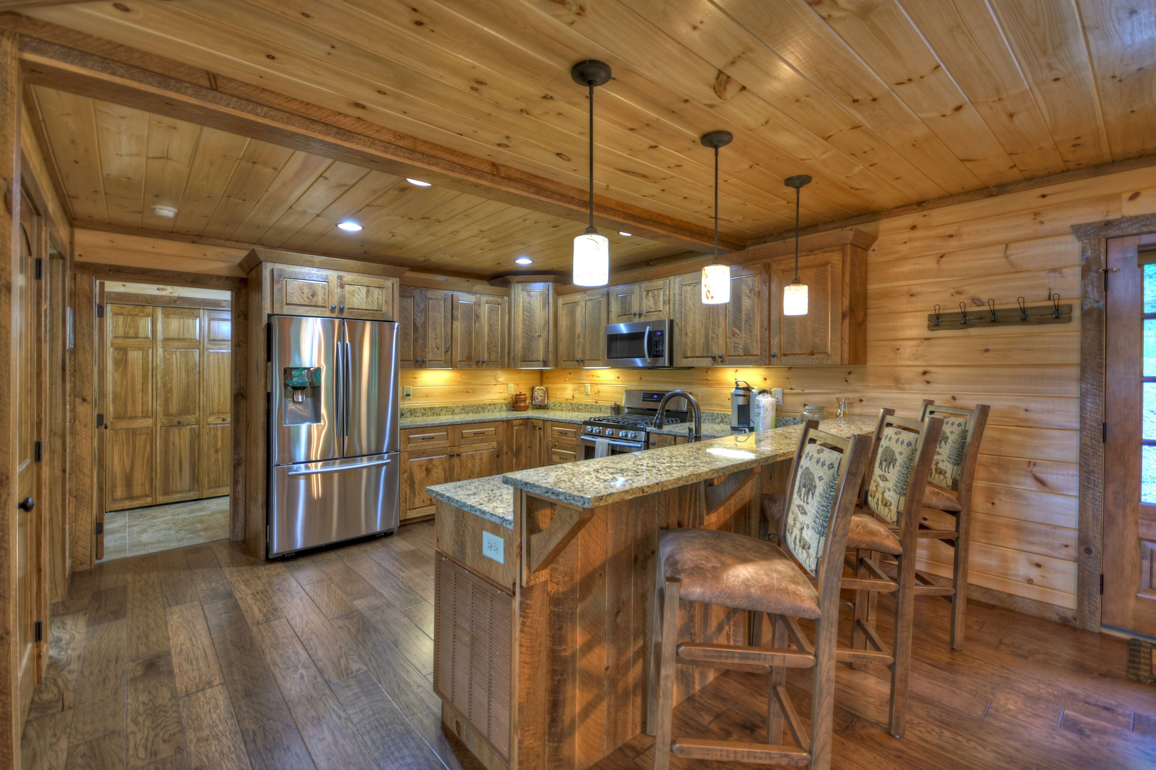 A wooden cabin-style kitchen with built-in appliances, a central island with bar stools, and pendant lighting.