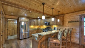 A wooden cabin-style kitchen with built-in appliances, a central island with bar stools, and pendant lighting. - Deer Trails Cabin - Blue Ridge (Cherry Log)
