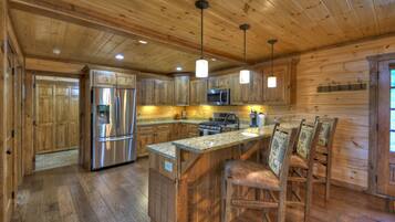A wooden cabin-style kitchen with built-in appliances, a central island with bar stools, and pendant lighting.