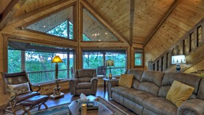A spacious living room with large windows, wooden beams, and leather furniture. - Deer Trails Cabin - Blue Ridge (Cherry Log)