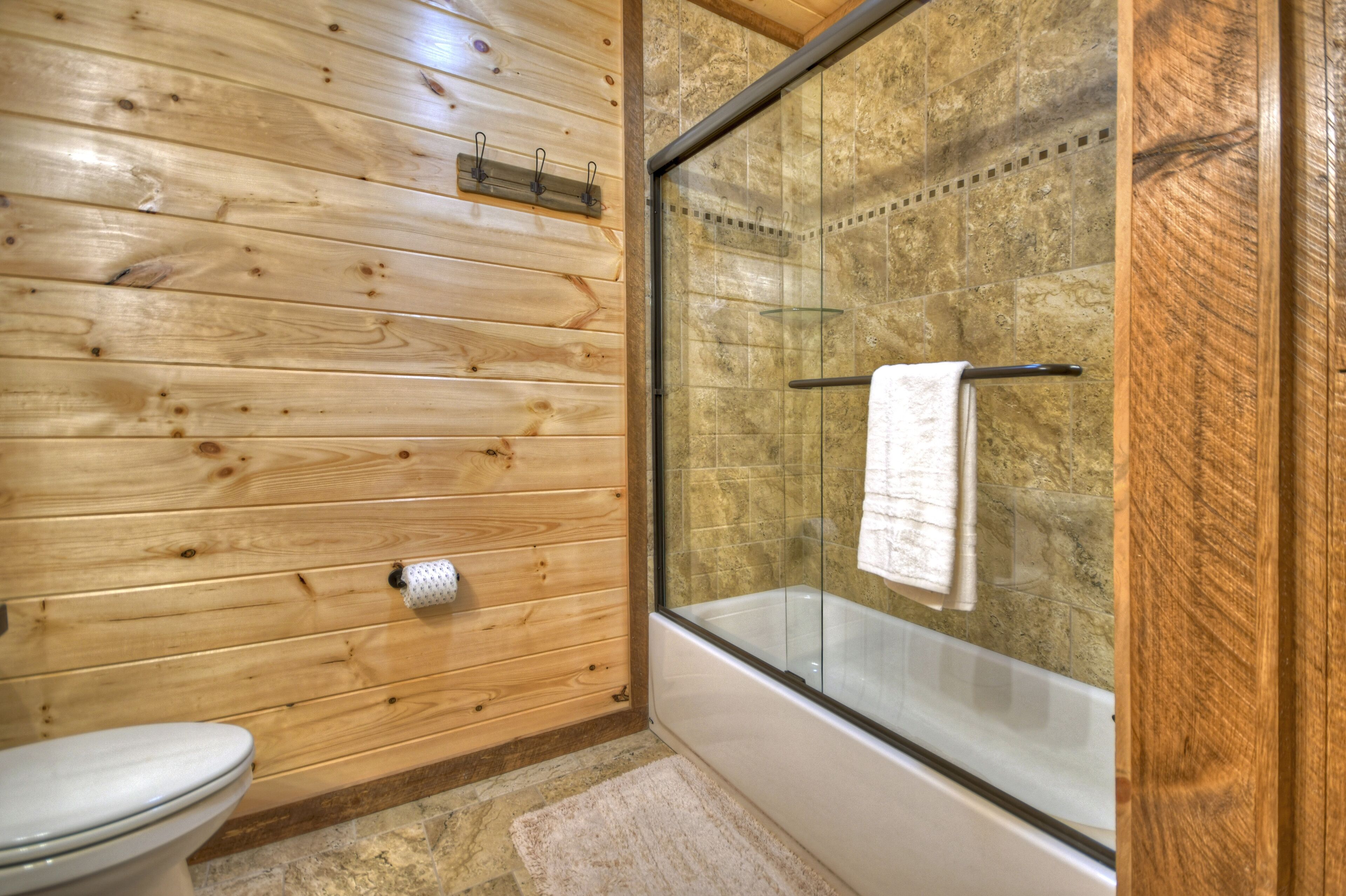 A wooden-paneled bathroom with a glass shower enclosure and a white bathtub.