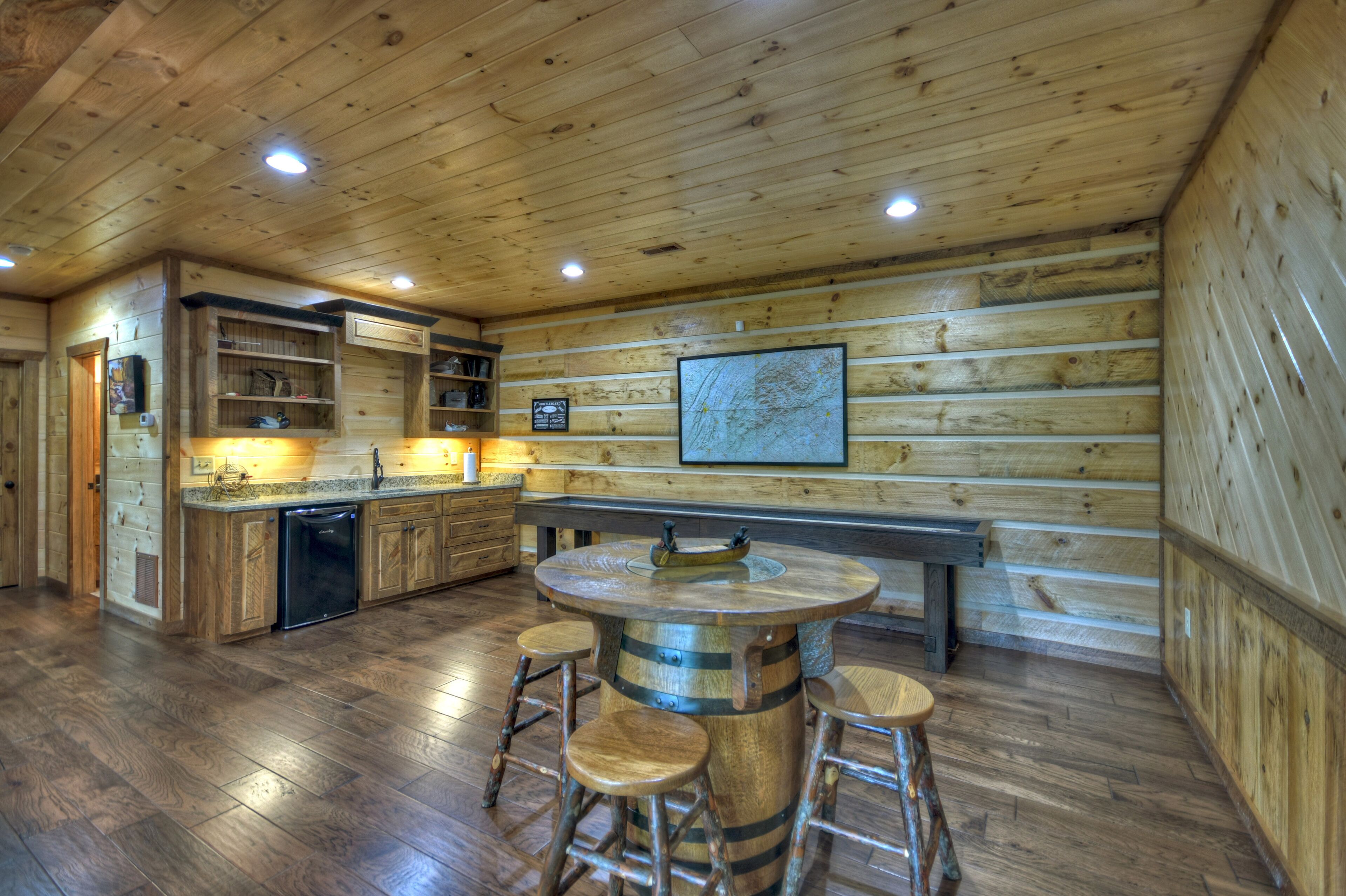 Un intérieur rustique en bois, avec un coin cuisine comprenant des meubles de rangement en bois, un lave-vaisselle encastré et une table ronde en bois, accompagnée de tabourets.