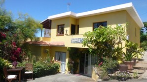 A two-story yellow house with a balcony, surrounded by various plants and flowers. - Apartment Rosa 1 - Apartments Rosa (Tijarafe)