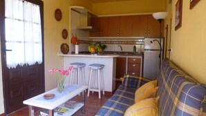 A compact living space with a kitchenette, a sofa, a dining table, and a window with curtains. - Apartment Rosa 1 - Apartments Rosa (Tijarafe)