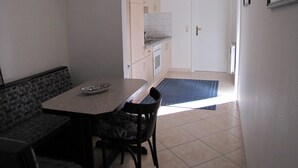 Une petite cuisine propre, avec un coin repas, une horloge au mur et une porte donnant sur une autre pièce.