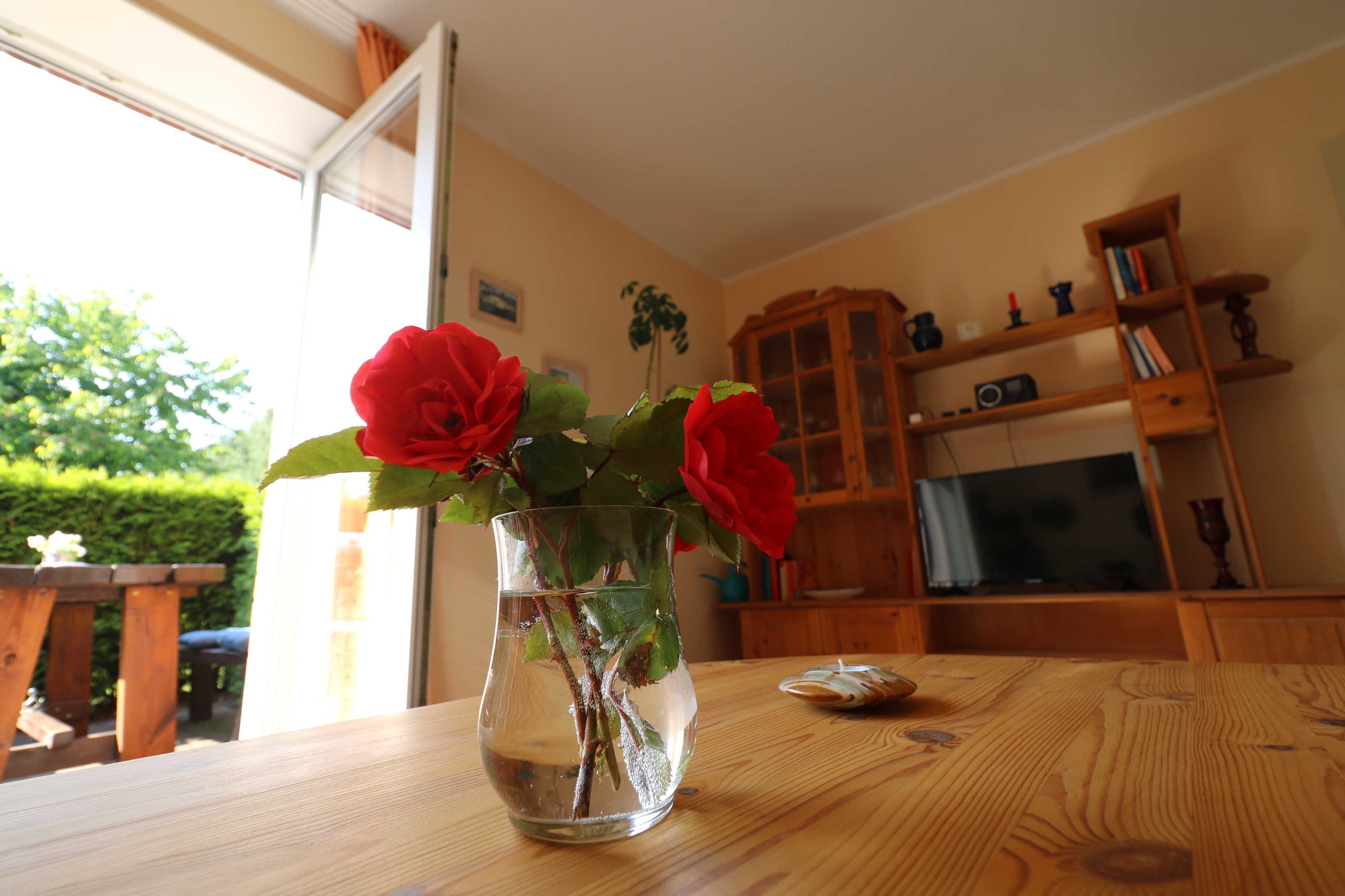 Una mesa de madera con un jarrón de rosas rojas, un aparador de madera y un televisor en una habitación con paredes color beige.